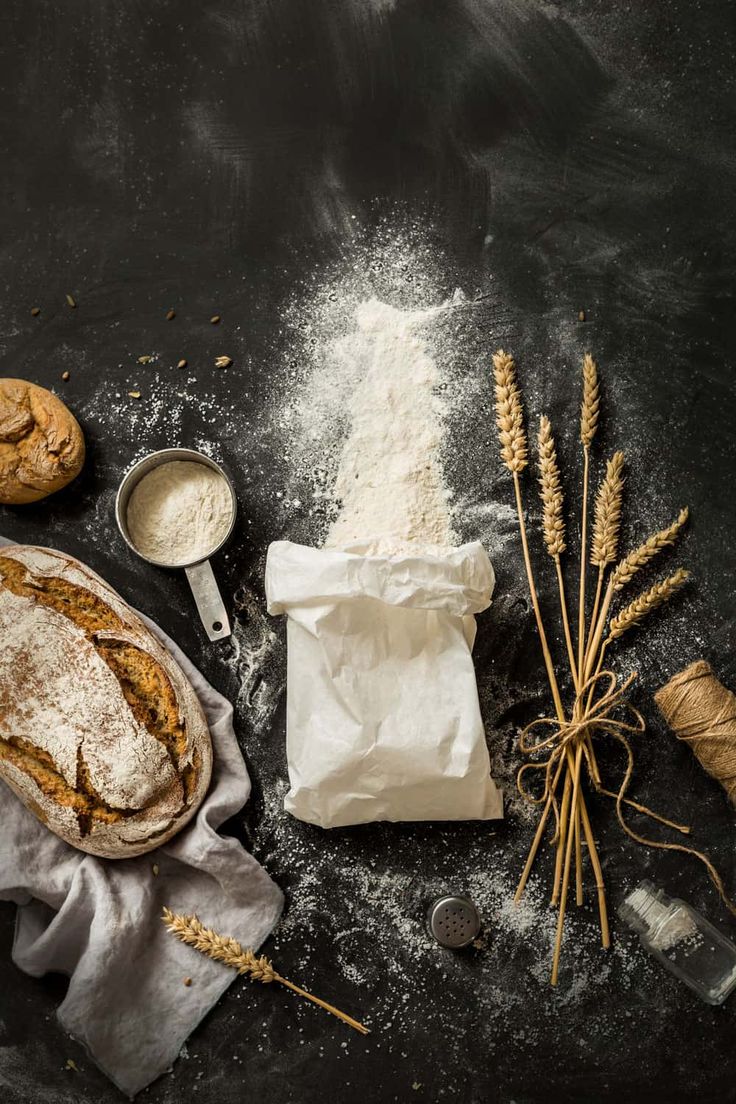 bread, flour and baking utensils are laid out on a black table top