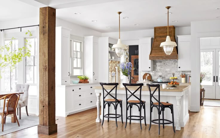 an open kitchen and dining room with white cabinets, wood flooring and pendant lights