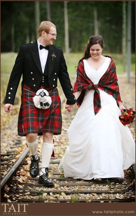 a man and woman dressed in kilts walking down train tracks holding each other's hands