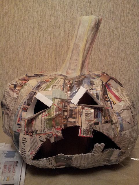 a paper mache pumpkin with newspaper pages cut out of it's face and mouth