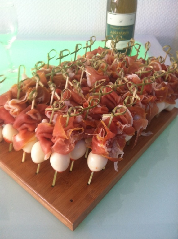 several skewered food items on a wooden platter next to a bottle of wine