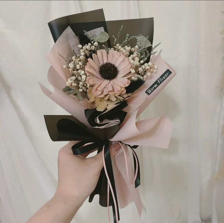 a hand holding a pink and black flower bouquet with ribbon around it's wrist