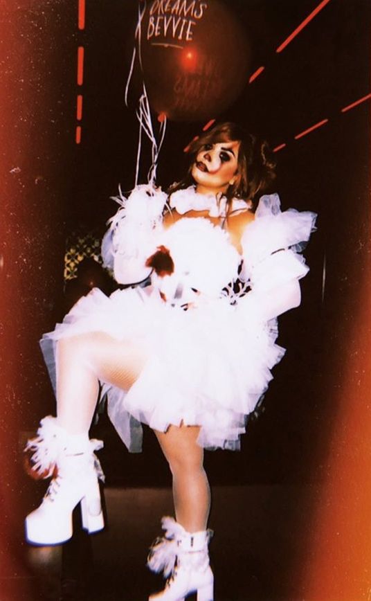 a woman dressed in white is holding a balloon and posing for the camera with her legs crossed