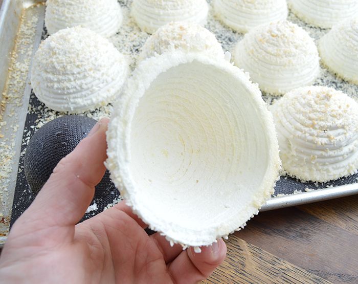 a person is holding up some white desserts on a baking sheet with other pastries in the background