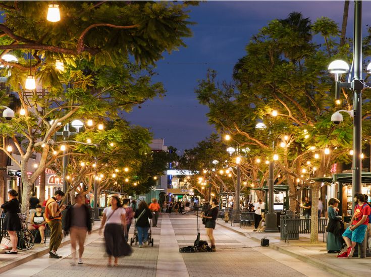 many people are walking down the street at night in an area with trees and lights