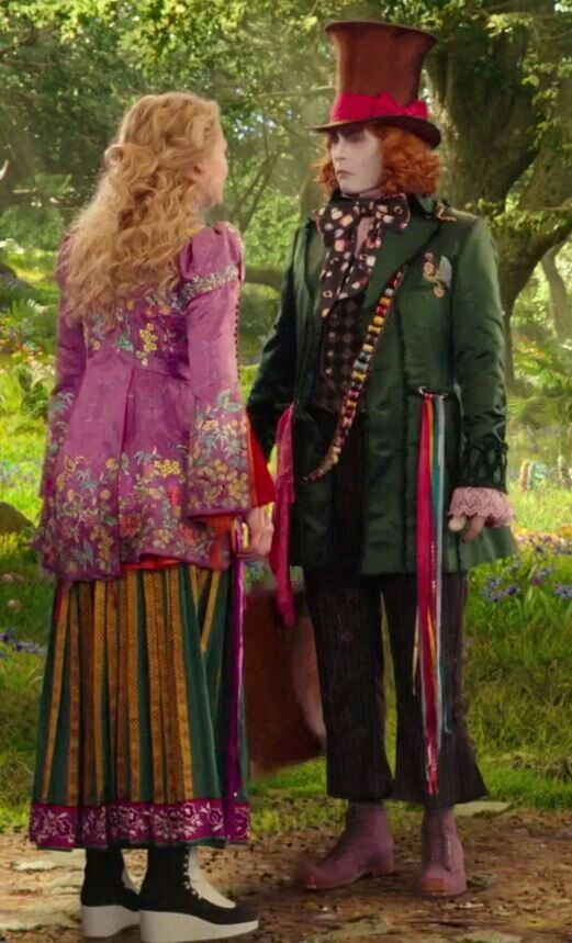 two people dressed in costume standing next to each other on a dirt road with trees and grass behind them