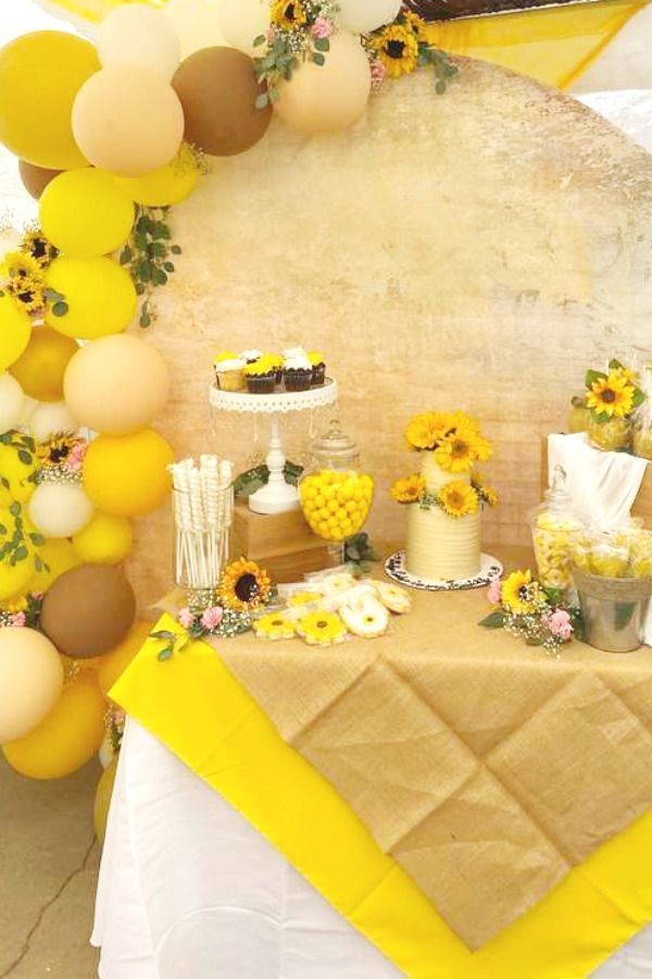 a table topped with yellow and white desserts next to a wall covered in balloons