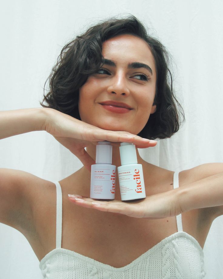 a woman holding two bottles of skin care products in front of her face and hands