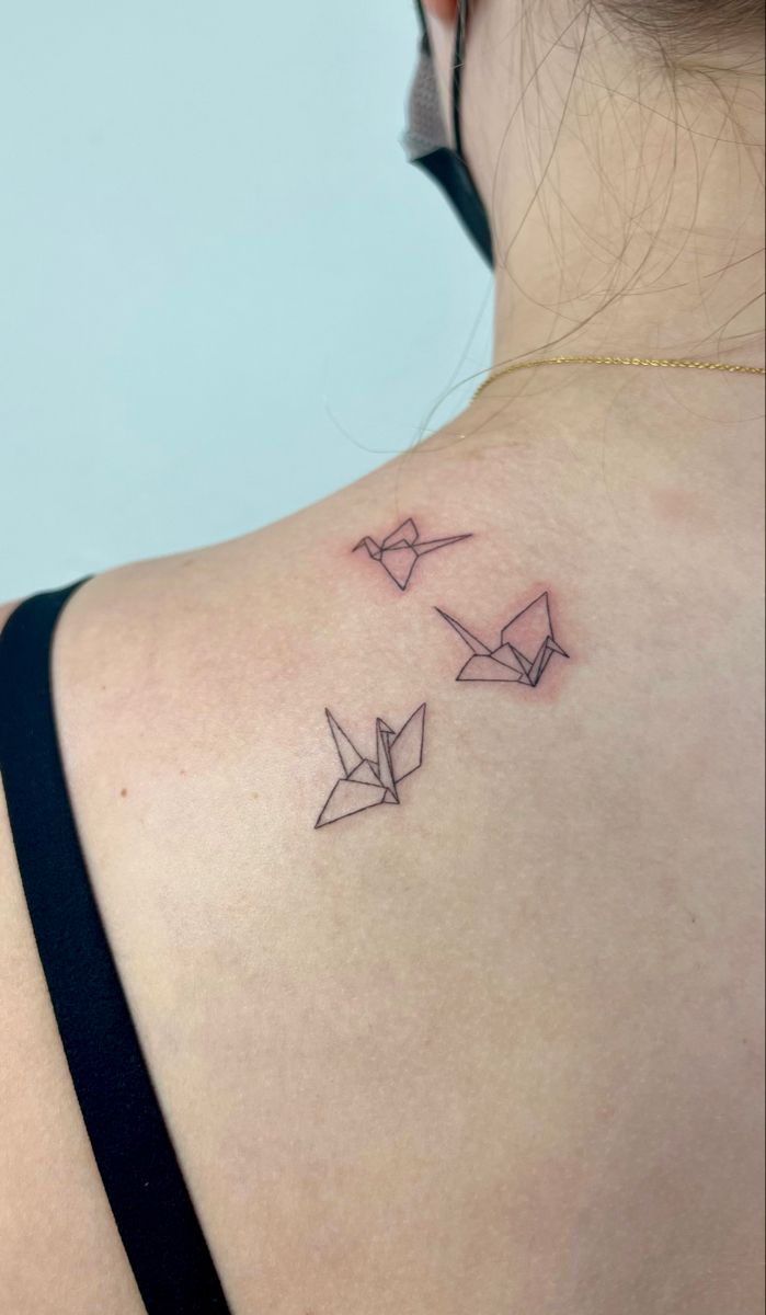 the back of a woman's shoulder with three origami birds on it