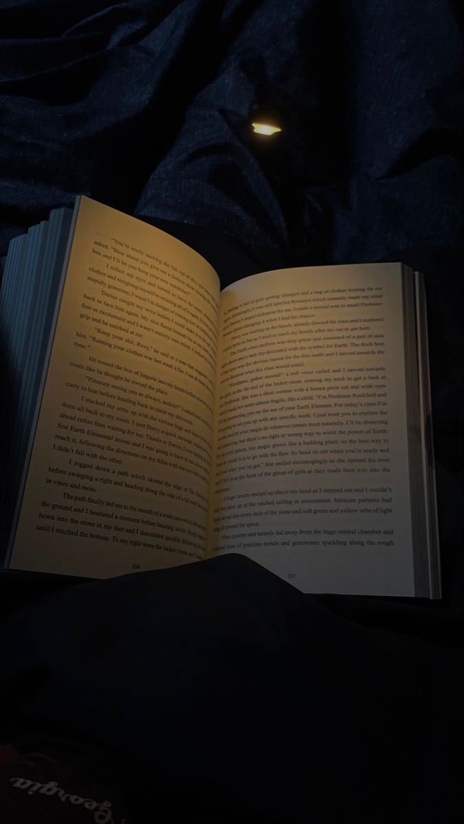 an open book sitting on top of a bed next to a light that is turned on