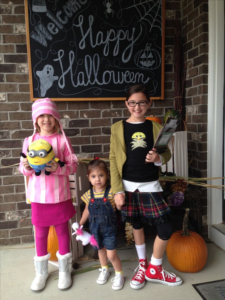 three children dressed up in costumes standing next to a chalkboard with the words happy halloween written on it