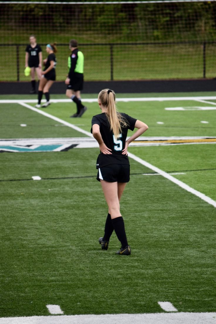 a woman standing on top of a lush green field next to a soccer ball court