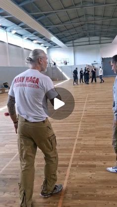 two men are standing in an empty room talking to each other and one man is wearing a white t - shirt