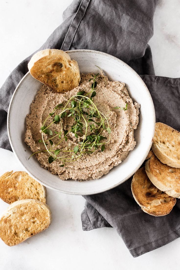 a white bowl filled with hummus and crackers on top of a gray napkin