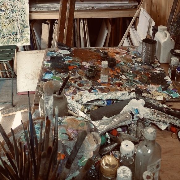 an artist's easel with lots of paint and brushes on it in a messy room