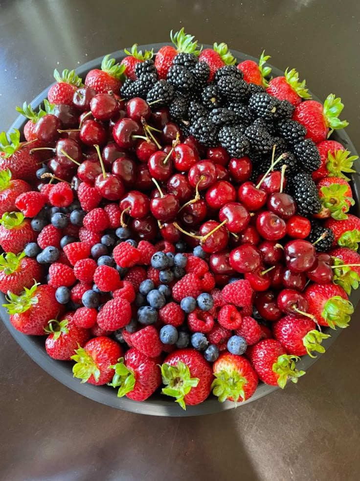 a bowl filled with berries and blackberries on top of a metal counter next to a sink