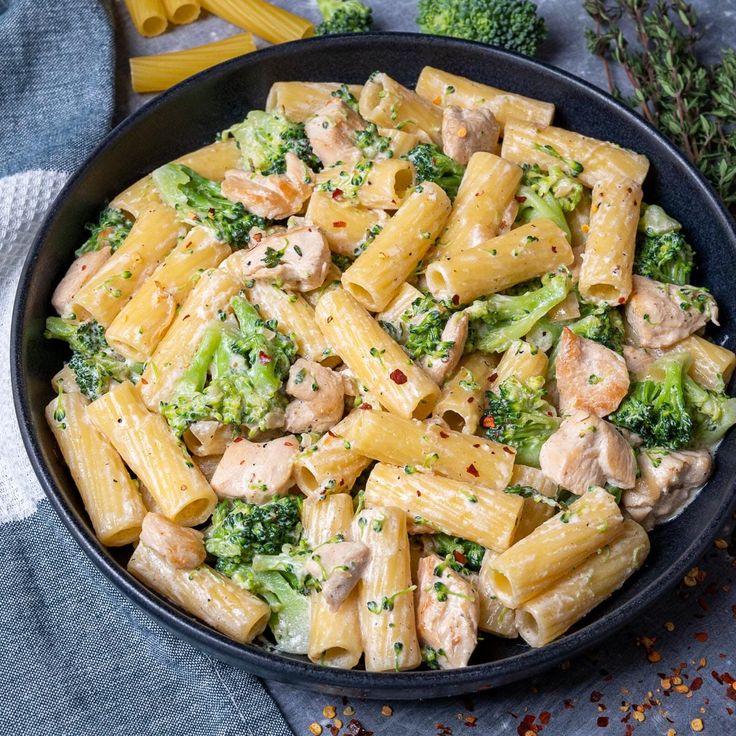 pasta with chicken and broccoli in a black bowl on a gray tablecloth