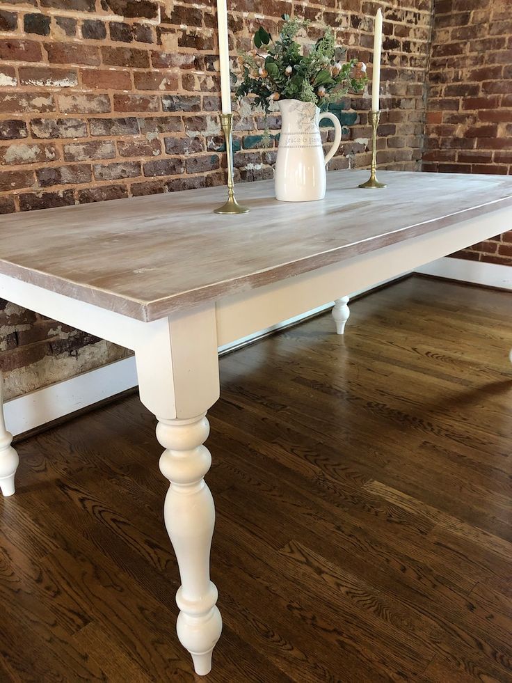 a white table with two candles on it in front of a brick wall and wooden floor