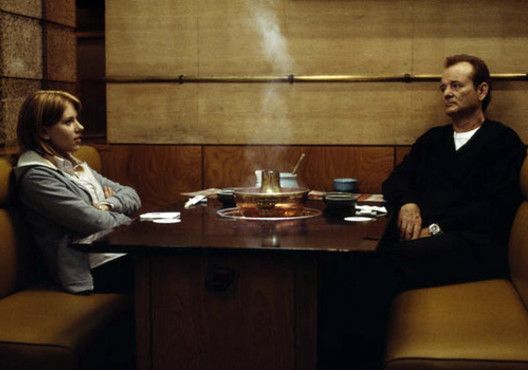 a man and woman sitting at a table in front of a wall with wooden paneling