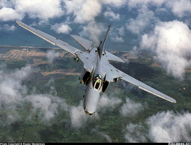 a fighter jet flying through the air above clouds and land in front of a forest