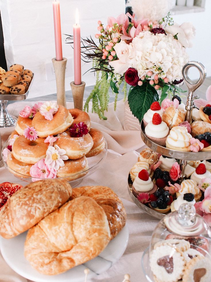 a table topped with lots of pastries and desserts next to a vase filled with flowers