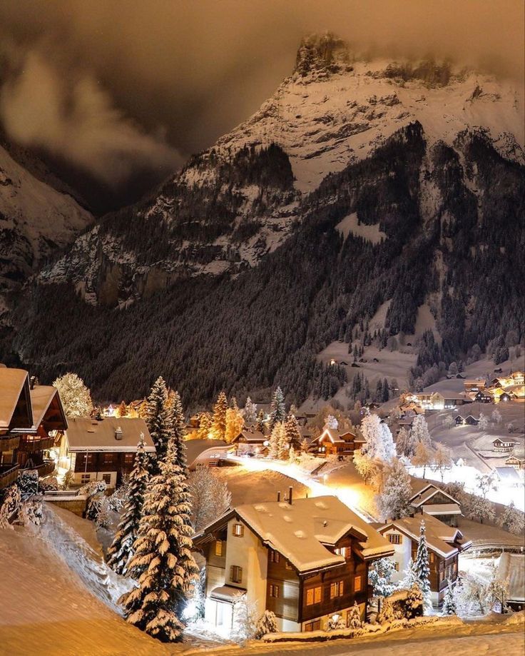 a snow covered mountain with houses in the foreground and lights shining on the mountains