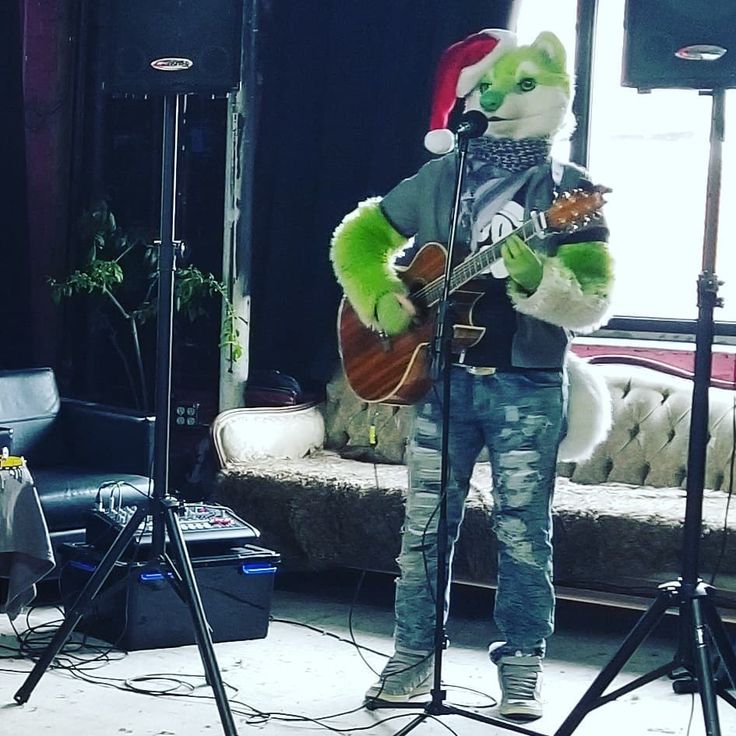 a man in a santa claus hat playing guitar and singing into a microphone while another person stands behind him