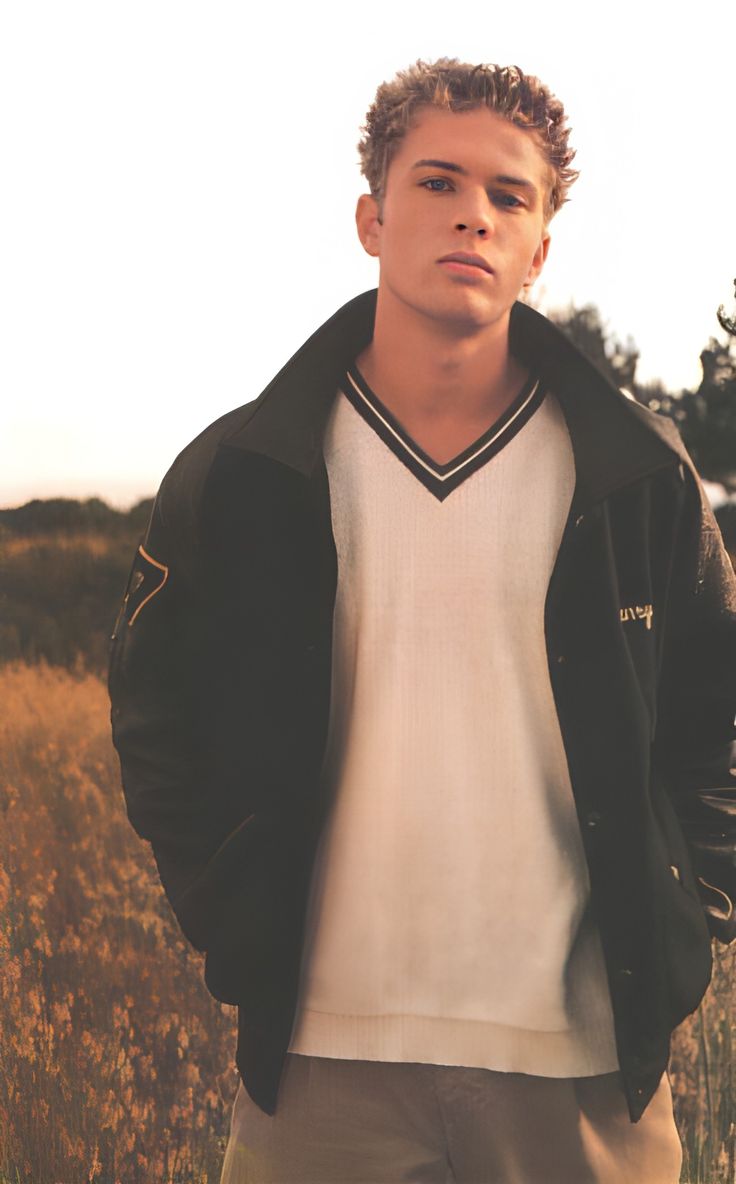 a young man standing in a field wearing a black jacket and white t - shirt