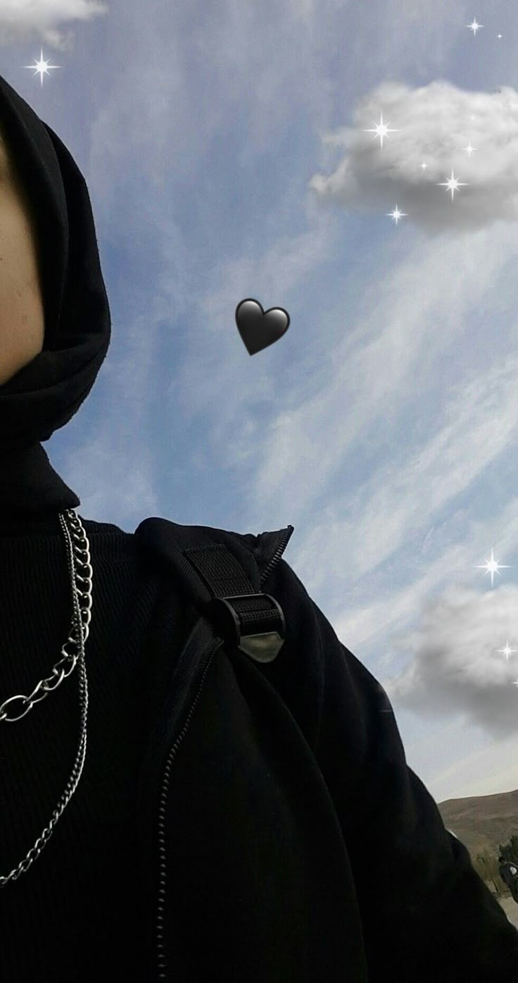 a person wearing a black hoodie with a heart shaped object in the sky behind them