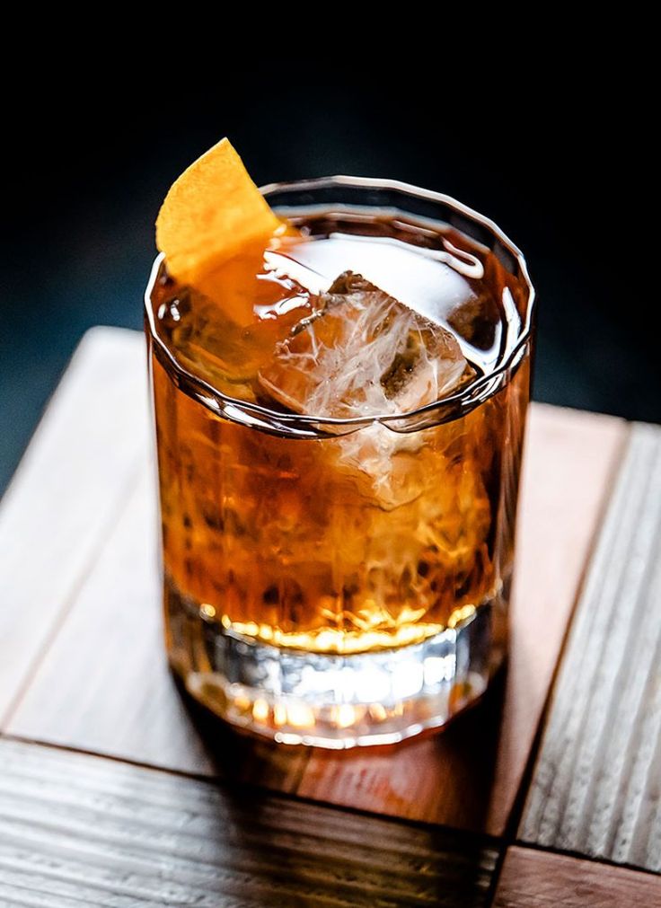 a close up of a drink on a wooden table with ice and an orange peel