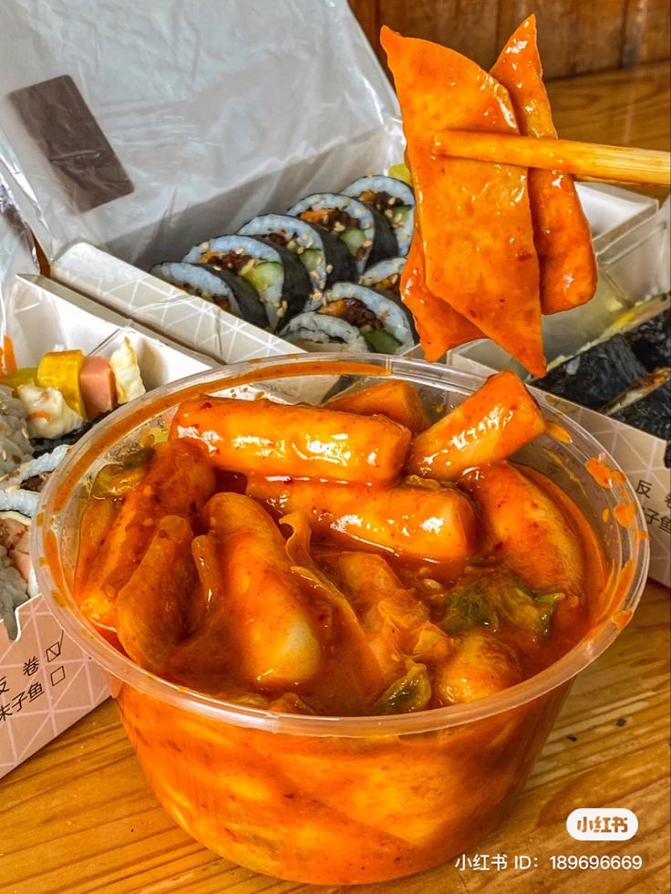 a bowl filled with lots of food sitting on top of a wooden table next to sushi