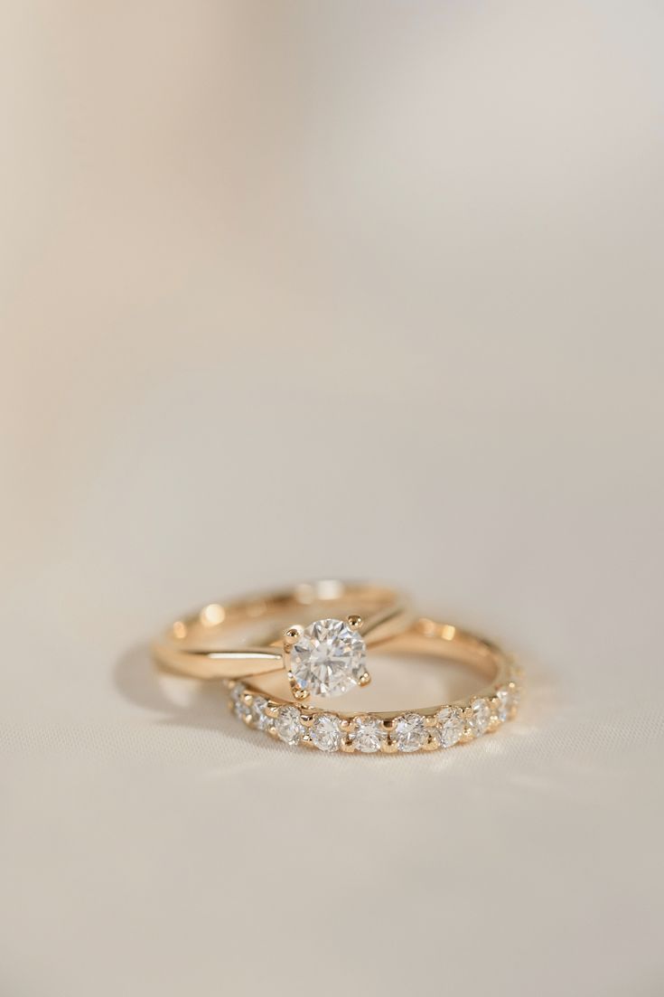 two gold wedding rings with white diamonds on the top and bottom, sitting on a table