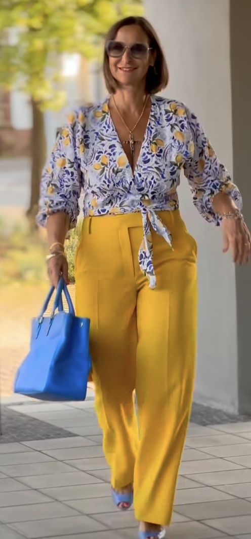 a woman walking down the street carrying a blue bag and wearing yellow pants with floral prints