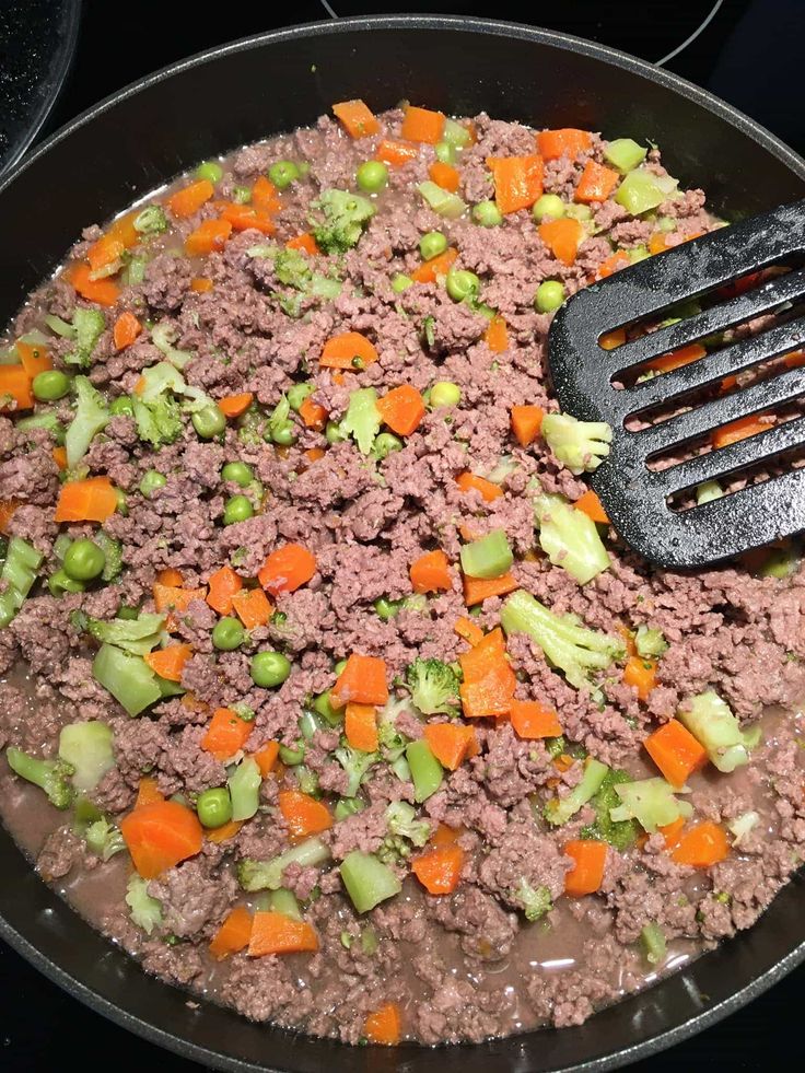 meat and vegetables being cooked in a skillet on the stove with a spatula