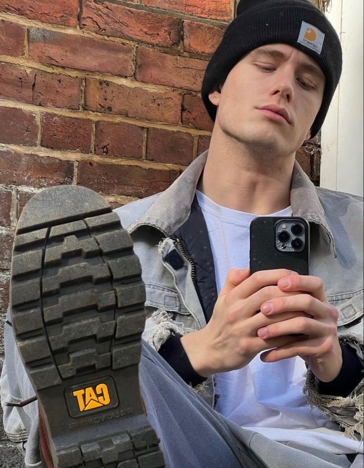 a young man sitting on the ground looking at his cell phone