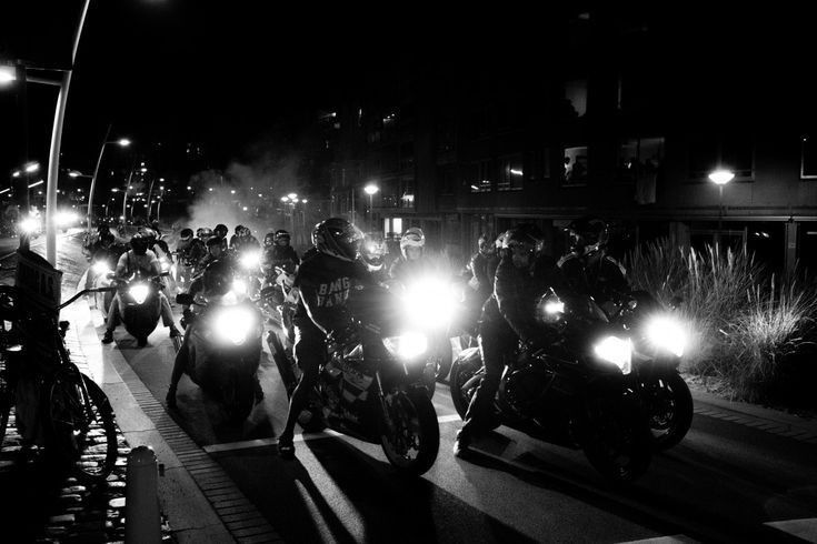 a large group of motorcyclists riding down the street at night with their headlights on