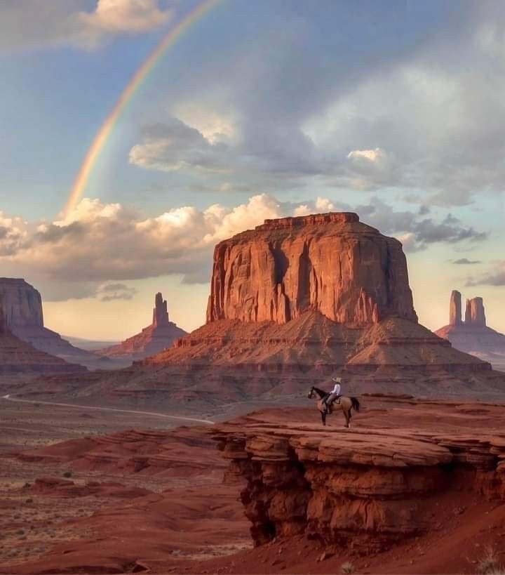 a man riding a horse across a desert landscape with a rainbow in the sky above