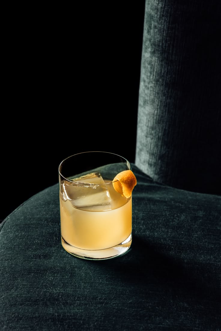 Yellow cocktail in a short clear glass with large ice cube and orange peel sitting on a green velvet sofa with black background Retro Cocktail Photography, Restaurant Cocktail Photography, Bar Photography Ideas, Winter Cocktail Photography, Espresso Martini Photography, Cocktail Foto, Drink Website, Cocktails Photography, Bar Photography