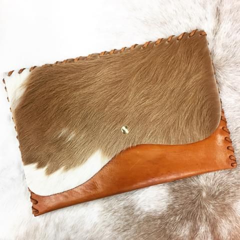 a brown and white cowhide with leather handle on a fur rug that looks like it has been cut in half