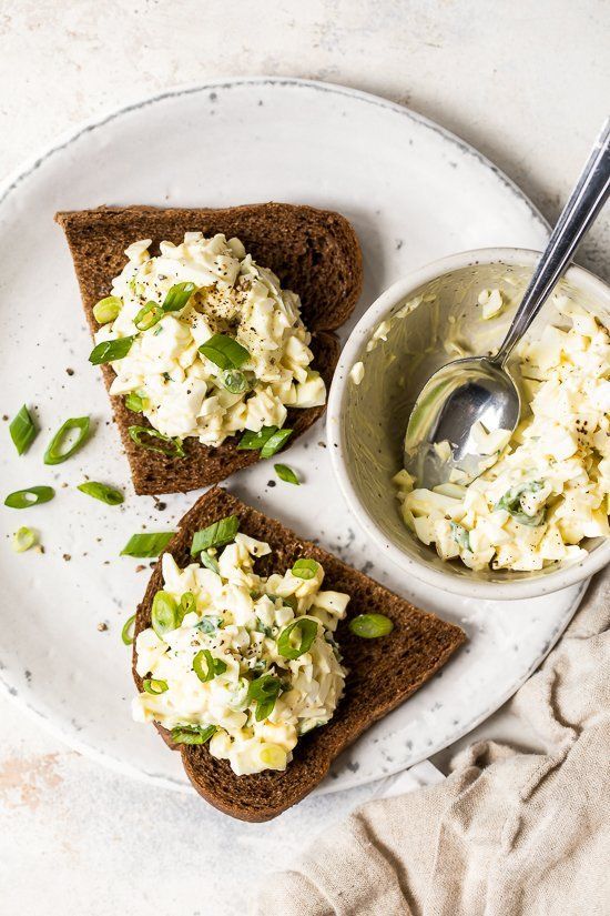 two pieces of toast with scrambled eggs on them and a bowl of yogurt