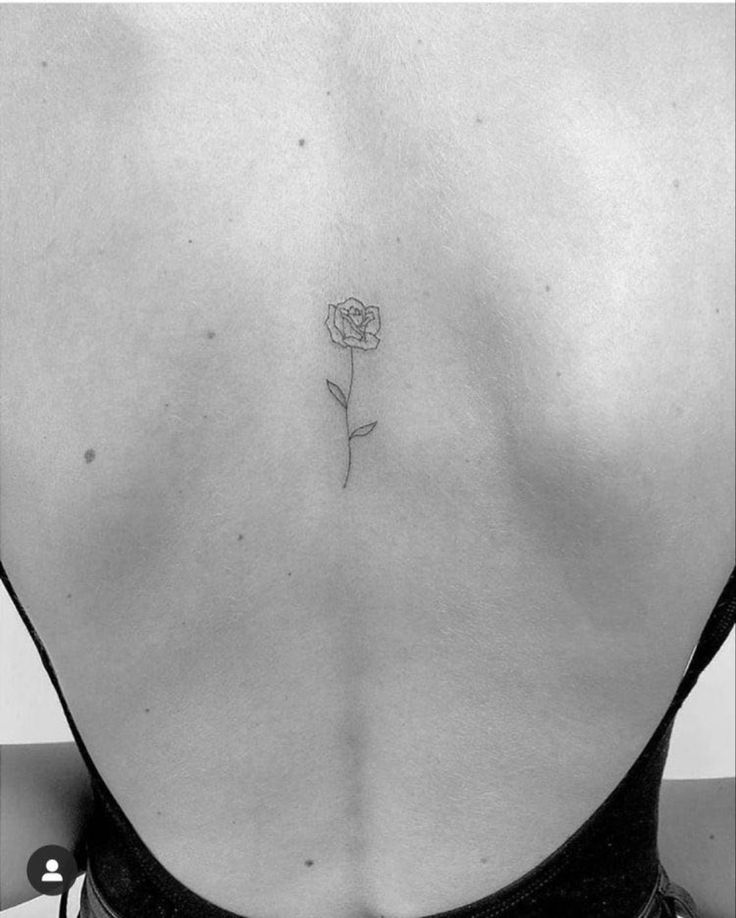 a woman's back with a single rose tattoo on her left side ribcage