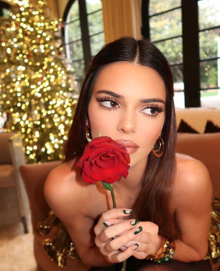 a woman sitting on top of a couch holding a red rose in her hand and looking at the camera