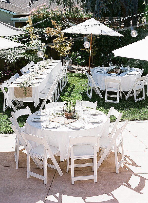 an outdoor dining area with white tables and chairs set up on the lawn, surrounded by umbrellas