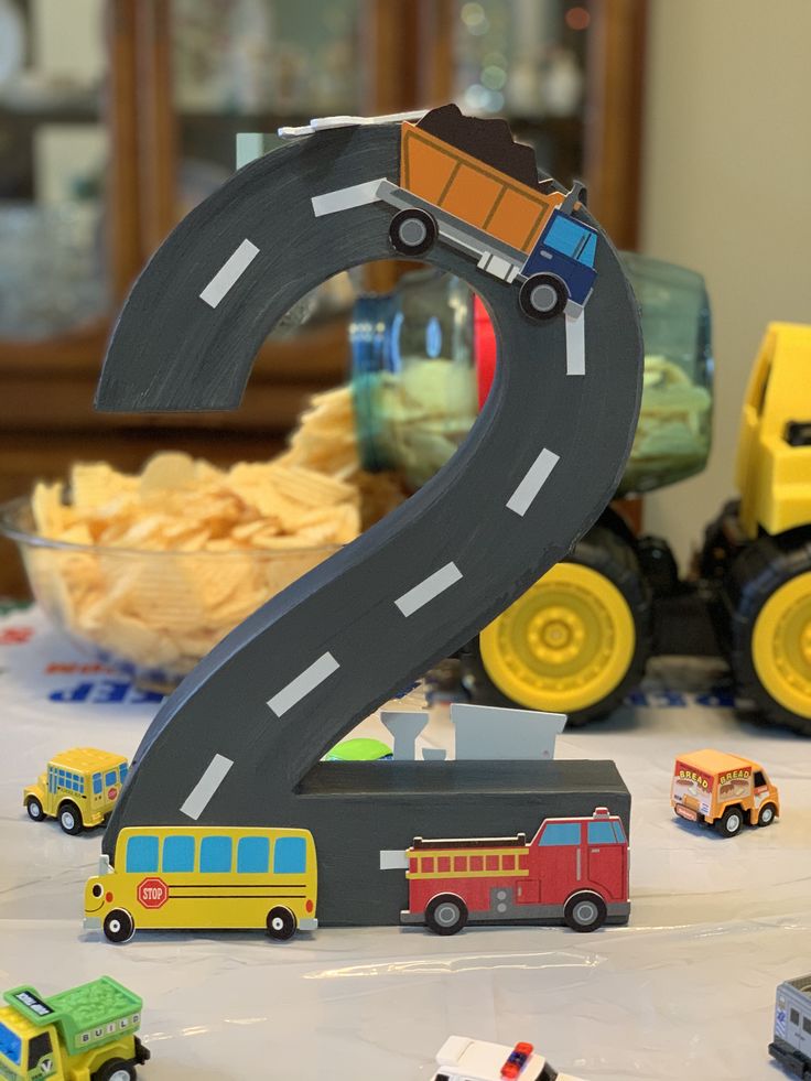 a table topped with toy cars and trucks next to a number 2 shaped like a road