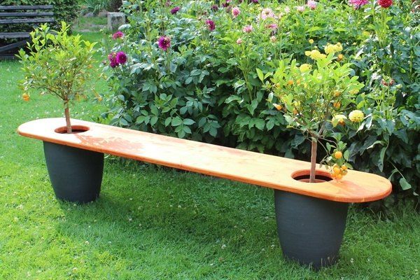 a wooden bench sitting in the middle of a lush green field next to bushes and flowers