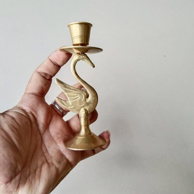 a hand holding a gold candle holder with a bird on it's side and a top hat on its head