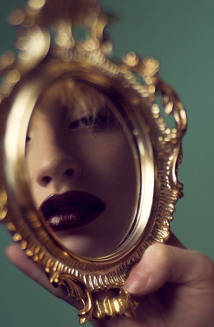 a woman's face is reflected in a gold framed mirror with her mouth open