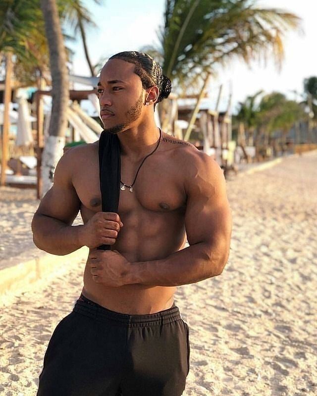 a shirtless man with no shirt on standing on the beach holding a black tie