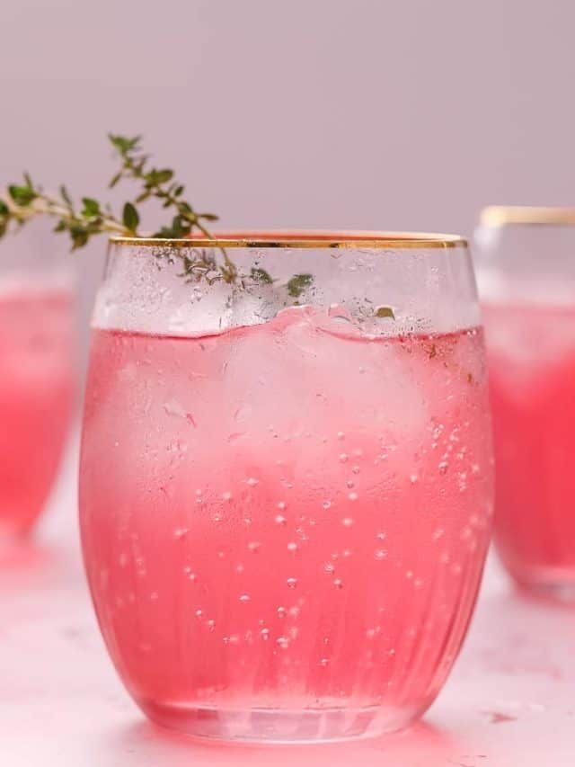 three glasses filled with pink liquid and garnished with greenery on the rim