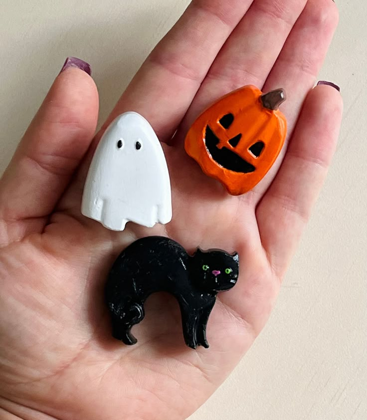 three halloween decorations in the palm of someone's hand, one black cat and one white ghost